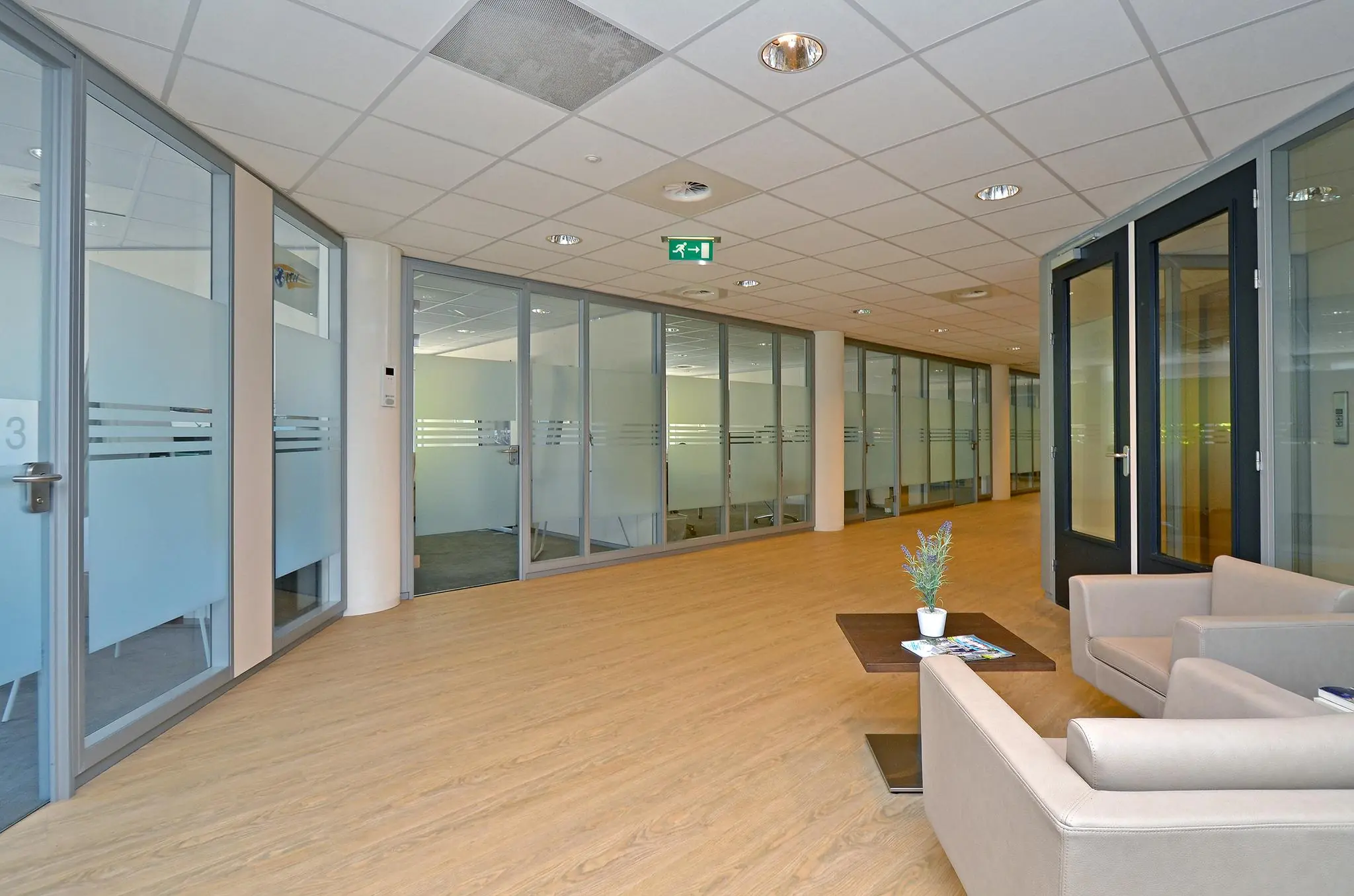 Moderne kantoorruimte aan de 1e Hogeweg met glazen vergaderruimtes en een wachthoek met stoelen en salontafel.